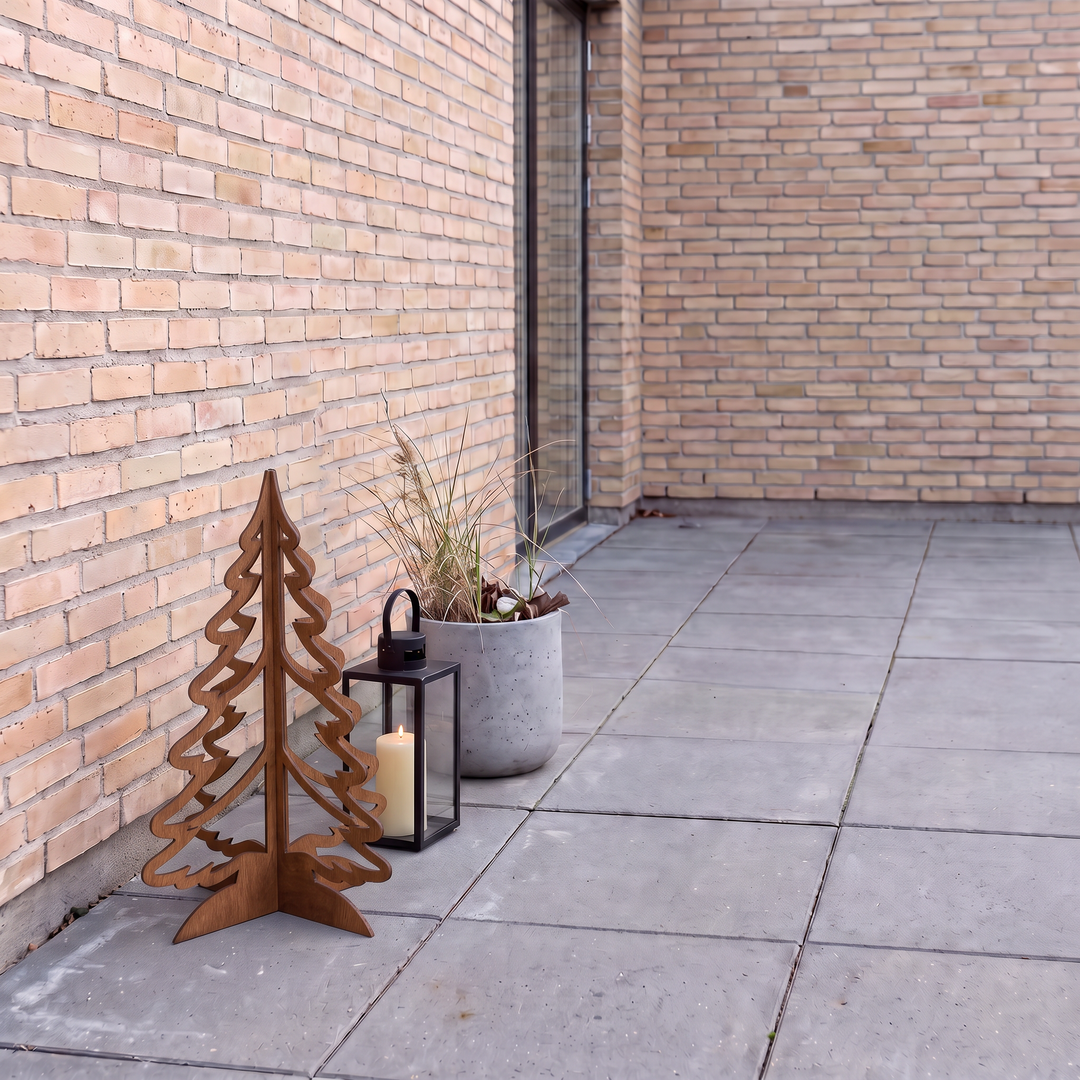 Deko-Tannenbaum mit Laterne und Pflanzkübel mit Gräsern auf grauen Terrassenplatten.