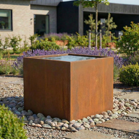 Eine höher Wasserbecken aus cortenstahl in einem schönen garten.  